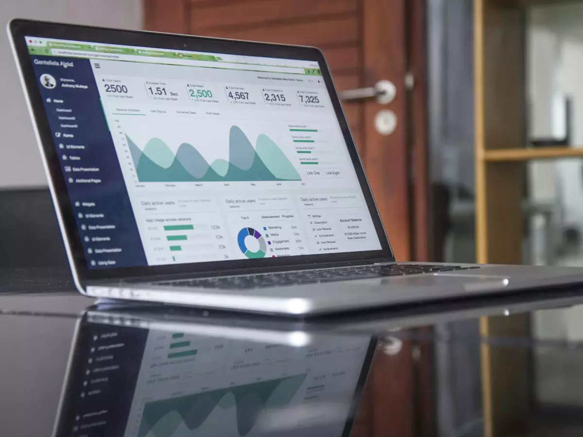 A laptop with a bright screen displaying graphs and charts, on a glass table.