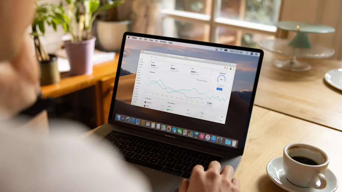 A person looking at graphs on a laptop screen in a home office.