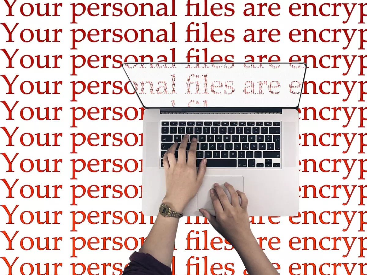 A person typing on a laptop with the text 'Your personal files are encrypted' repeated in red lettering all over the image.