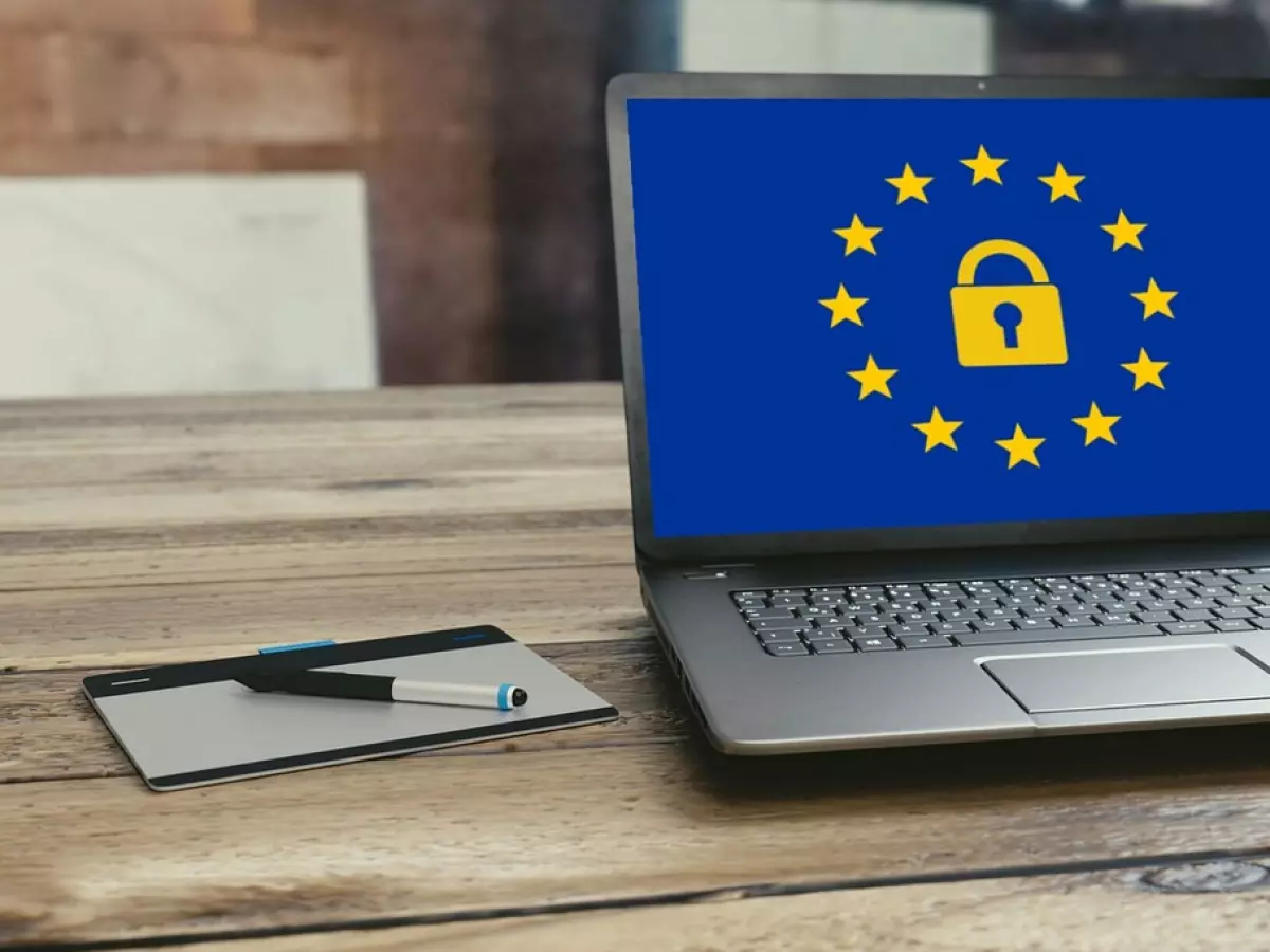 A laptop with a padlock icon on the screen, set against the backdrop of the EU flag, suggesting digital security and data protection.