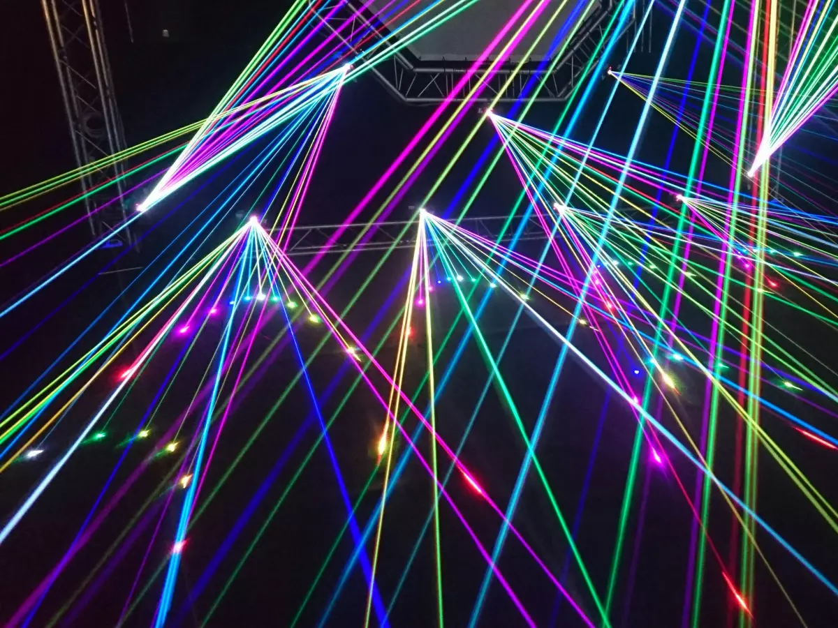 A dark background with multicoloured laser beams intersecting each other and creating a complex network of light. The beams are of different colours, creating a vibrant and abstract image.