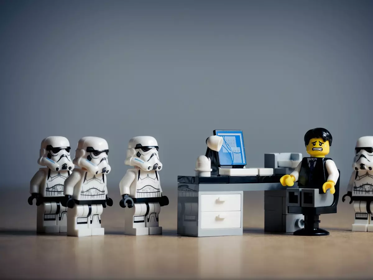 Lego minifigures of Star Wars characters, including stormtroopers and Darth Vader, stand around a desk with a man at a computer. The man looks distressed as if something bad has happened.