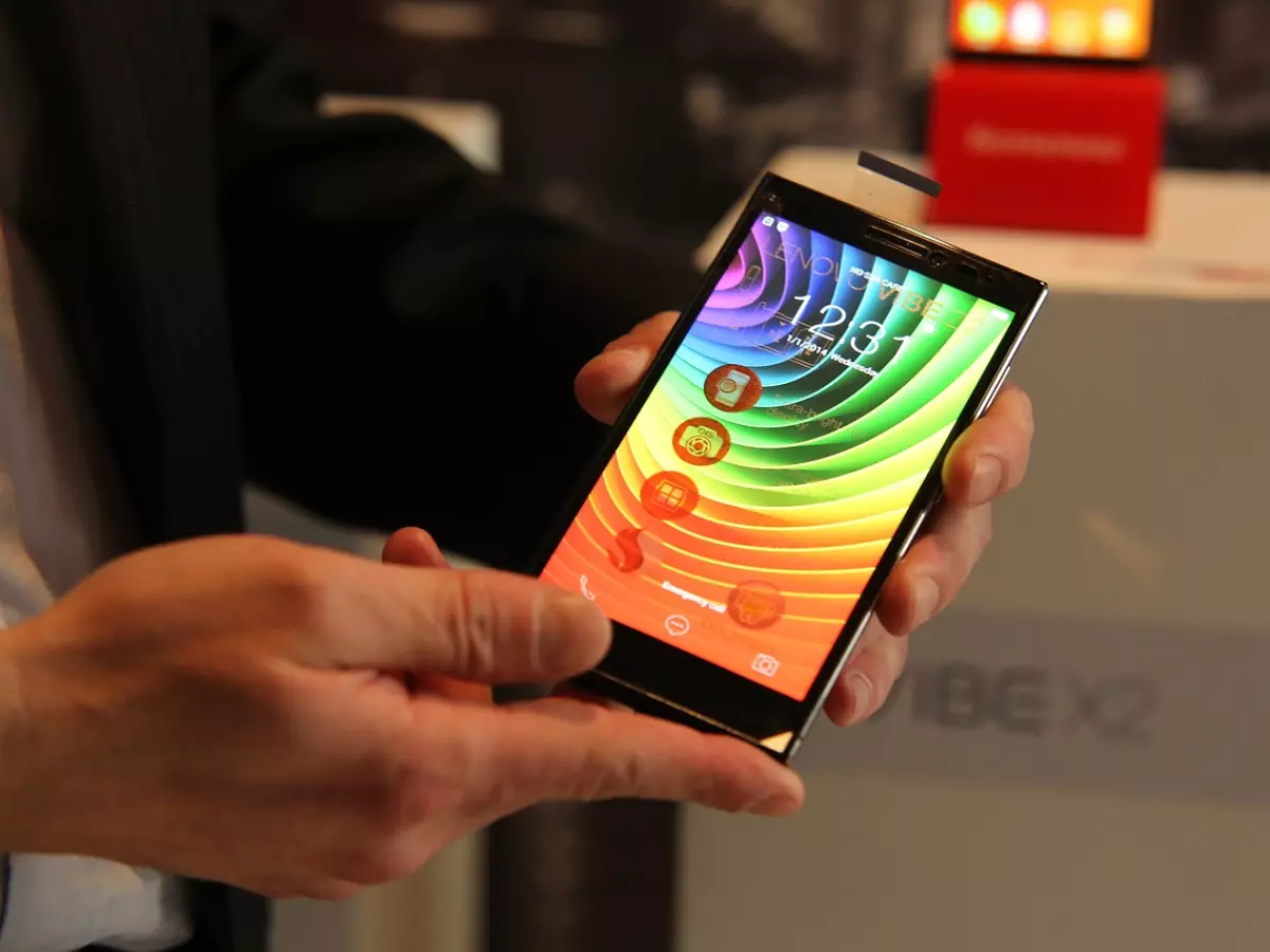 A person holding a black smartphone with a rainbow background.