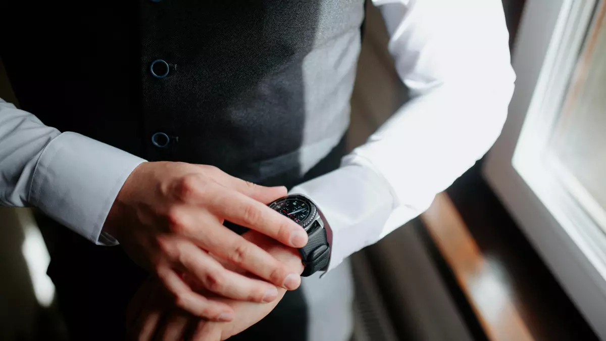 A man wearing a black smartwatch on his wrist. The watch is positioned in the center of the image and has a minimalist design. 