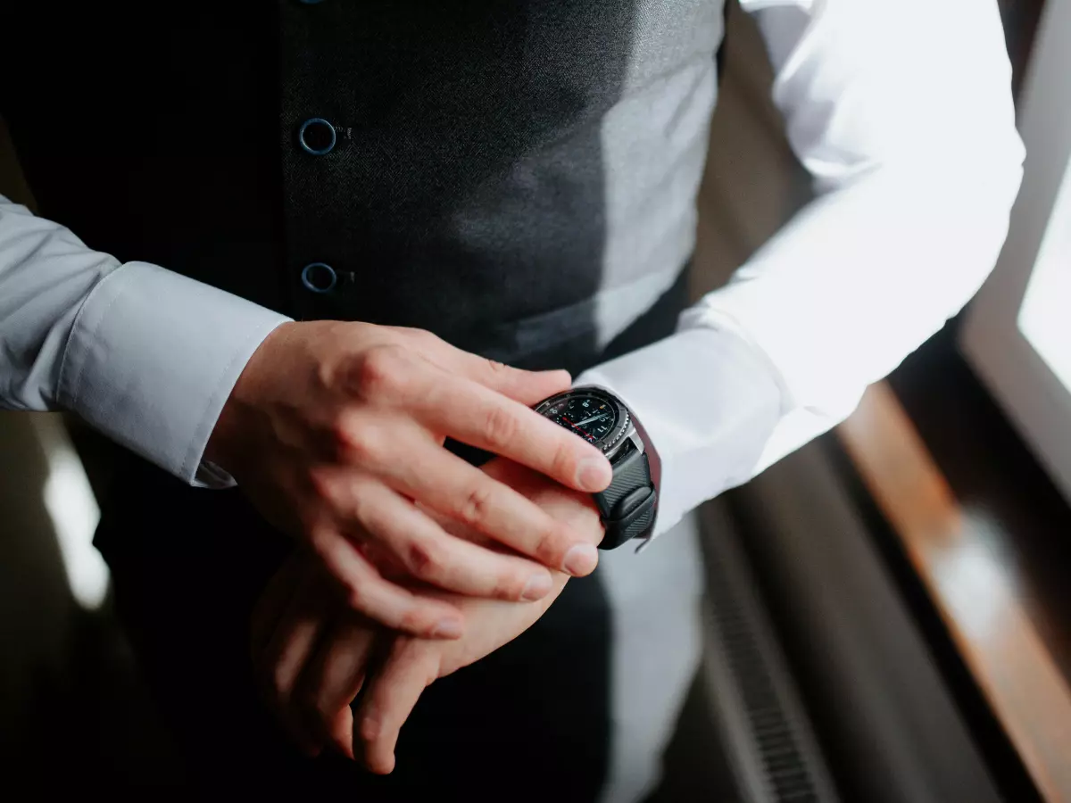 A man wearing a black smartwatch on his wrist. The watch is positioned in the center of the image and has a minimalist design. 