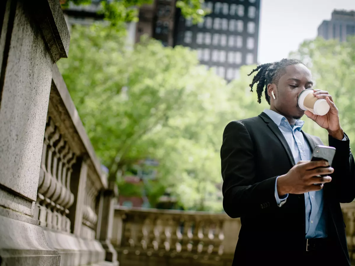 A man in a suit stands outside a building and looks at his phone.