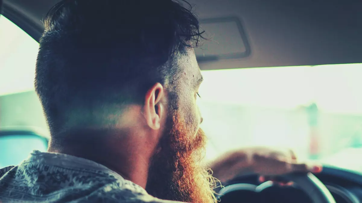 A close up shot of a bearded man driving a car.