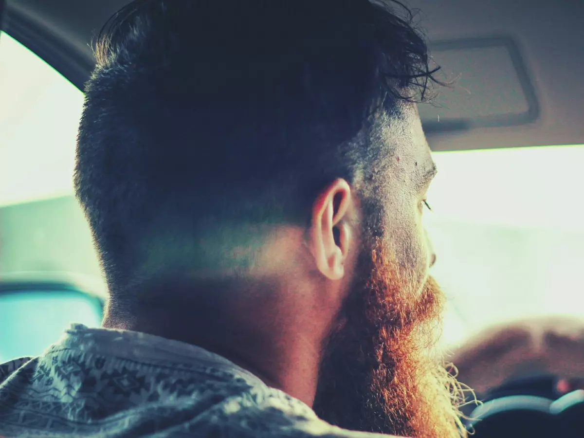 A close up shot of a bearded man driving a car.