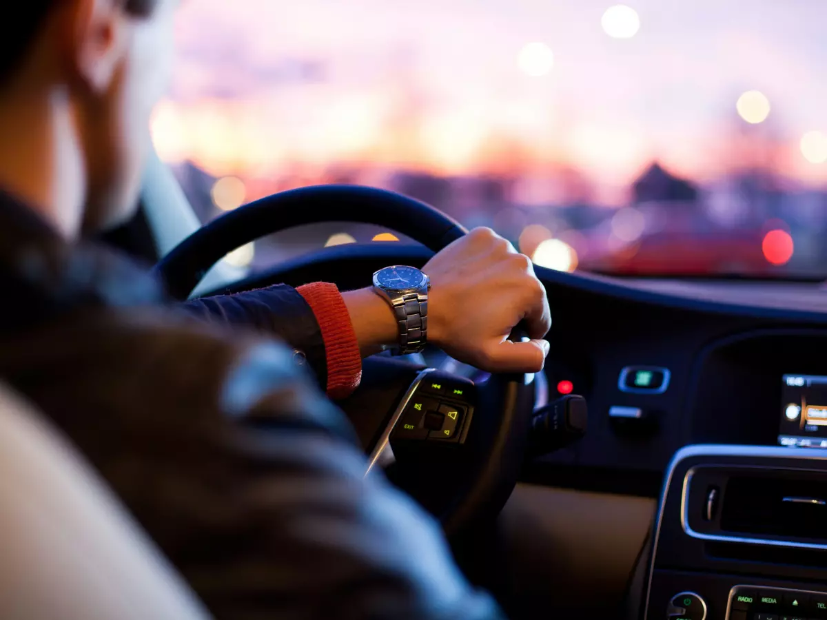 A person driving a car at night, the lights of the city are visible in the background.