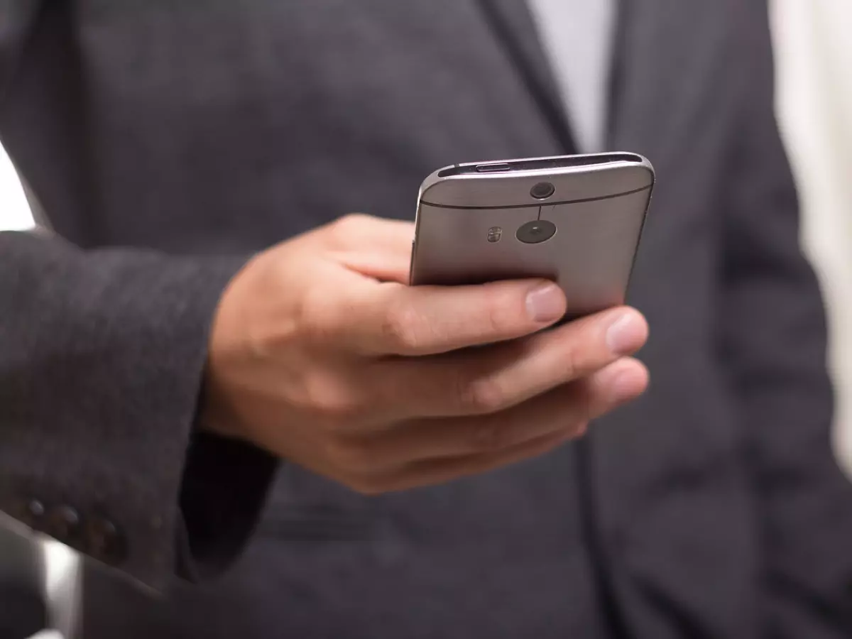 A close-up shot of a person's hand holding a smartphone, with a blurred background of a person wearing a suit.