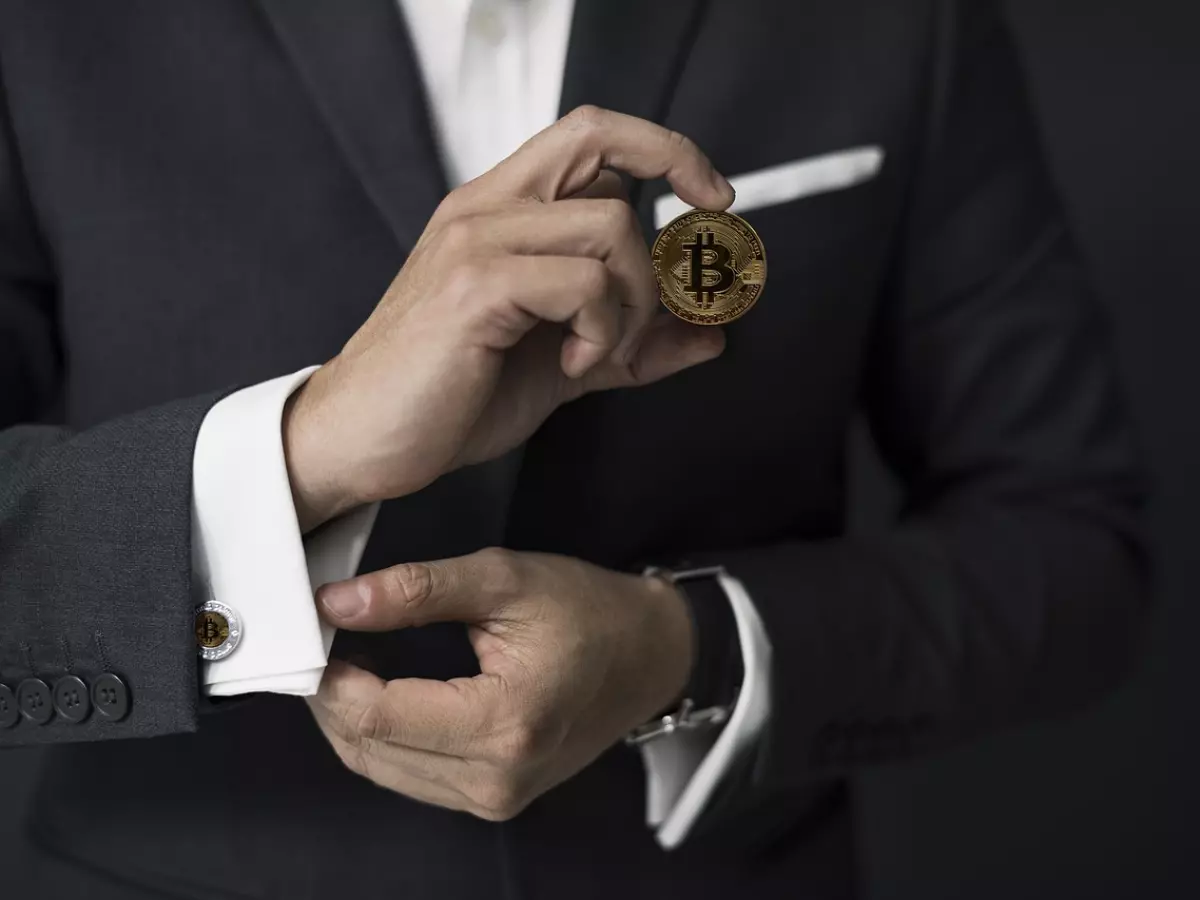 A man in a suit is holding a Bitcoin coin in his hand