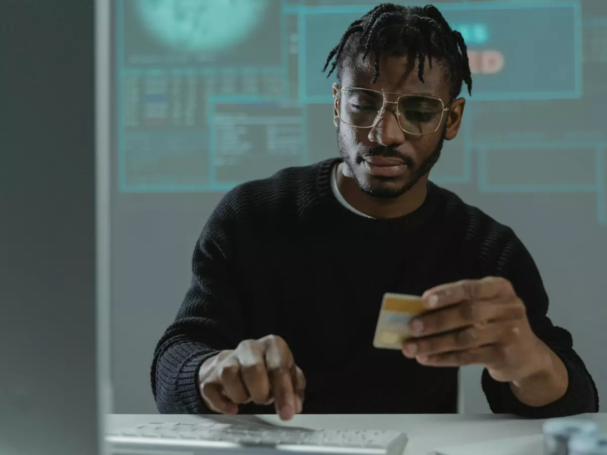 A man is sitting at a computer. He's looking at the screen and holding a credit card.