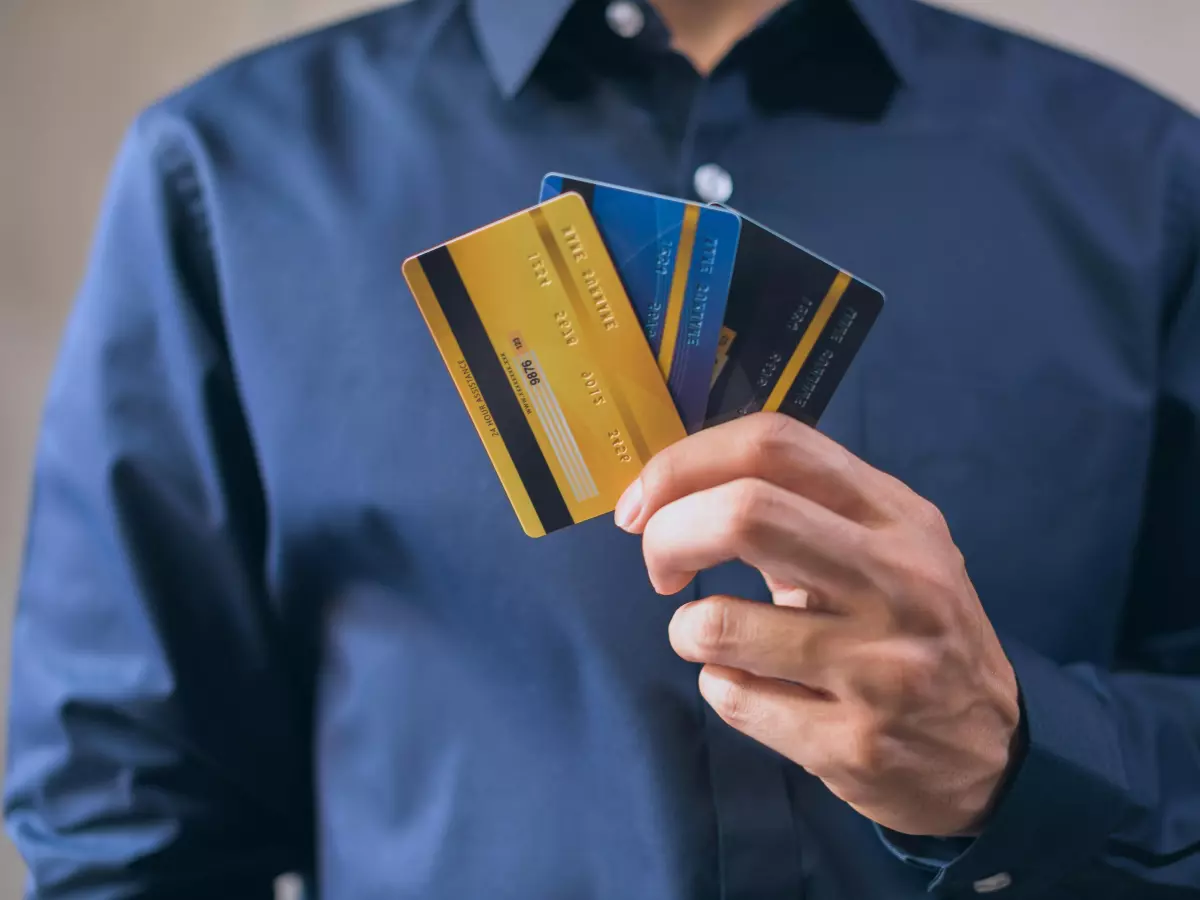 A man wearing a blue shirt is holding a stack of four credit cards in his right hand.