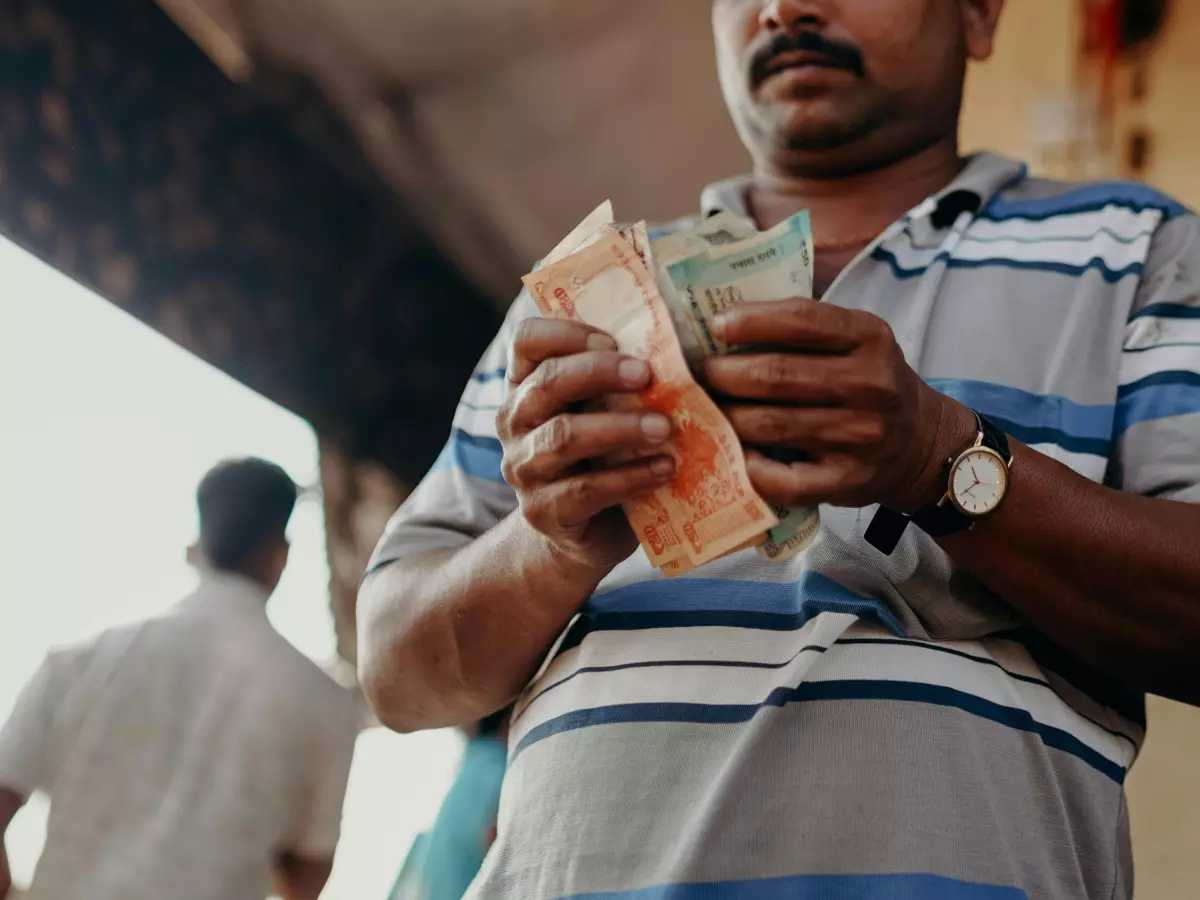 A man with a mustache holding Indian Rupees in his hands, blurred background