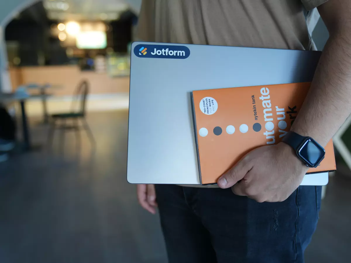 A person is holding a laptop and a book, the book says 'Automate Your Work'. 