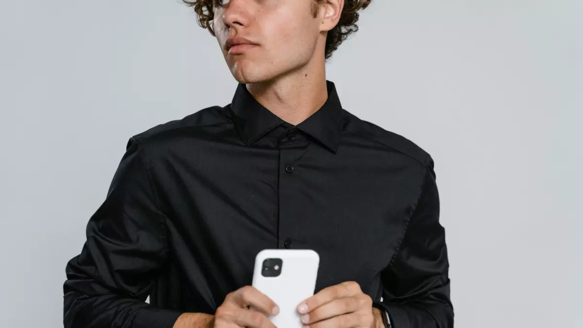 A man holding a white smartphone in his hands, looking away from the camera.