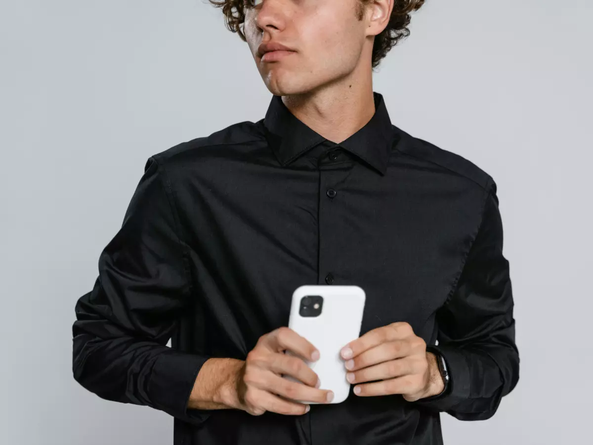 A man holding a white smartphone in his hands, looking away from the camera.