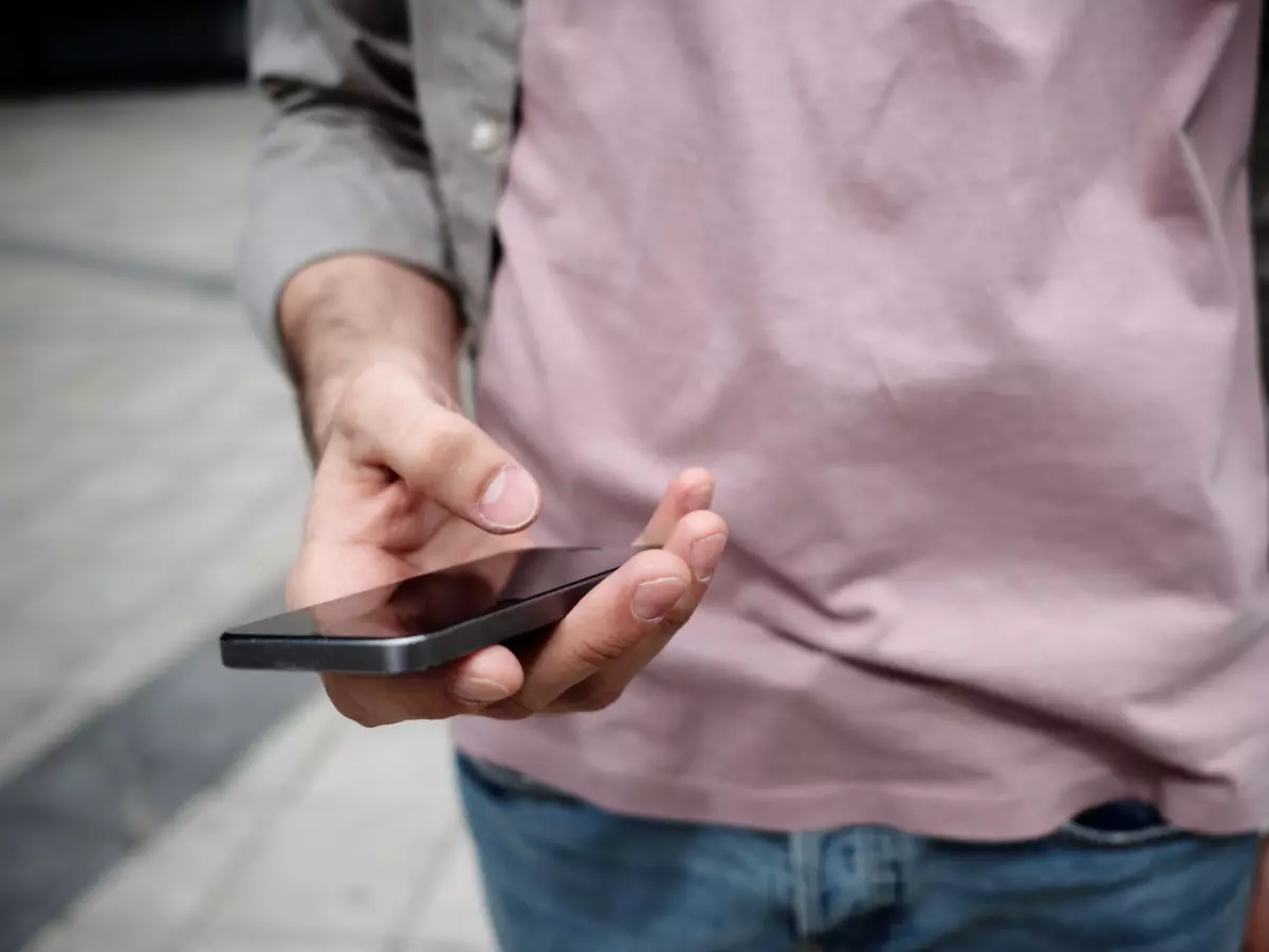 Close-up of a hand holding a smartphone, with the screen blurred, against a background of concrete tiles.