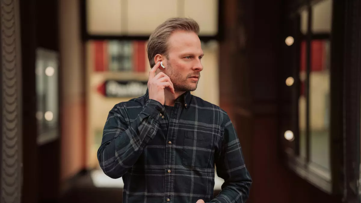 A man wearing AirPods Pro 2, standing in a hallway, adjusting the right earbud.