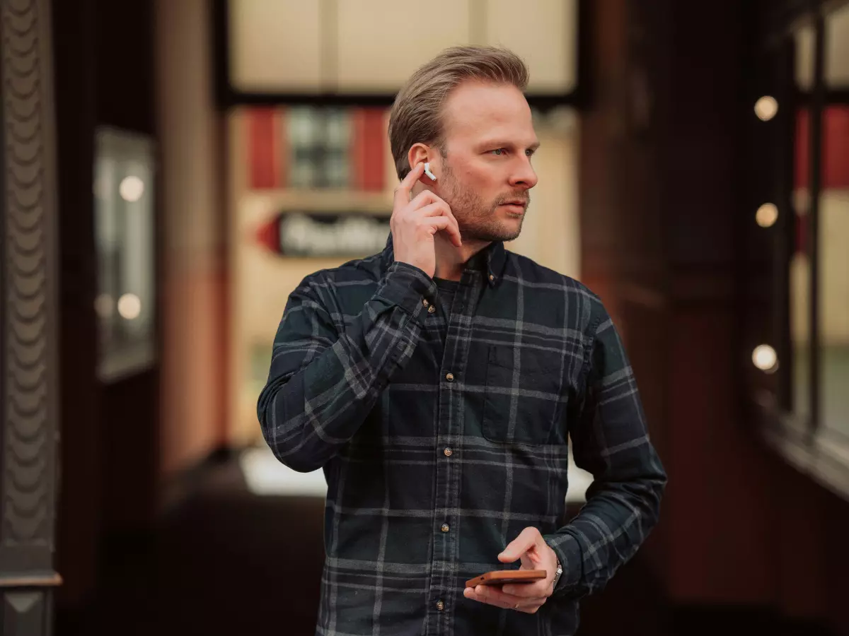 A man wearing AirPods Pro 2, standing in a hallway, adjusting the right earbud.