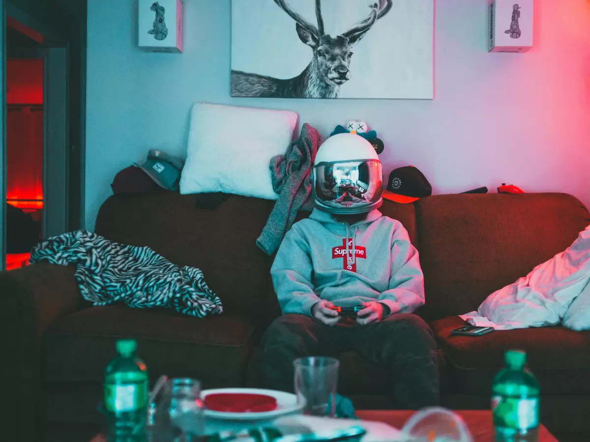 A person sitting on a couch in a dimly lit room, is wearing a futuristic helmet and playing a video game.