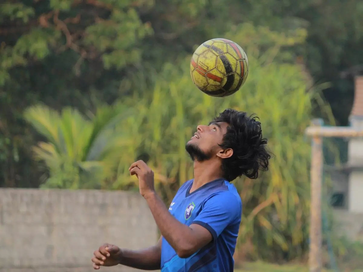 A young man is concentrating while controlling a ball with his head. He is playing soccer in a soccer field. 