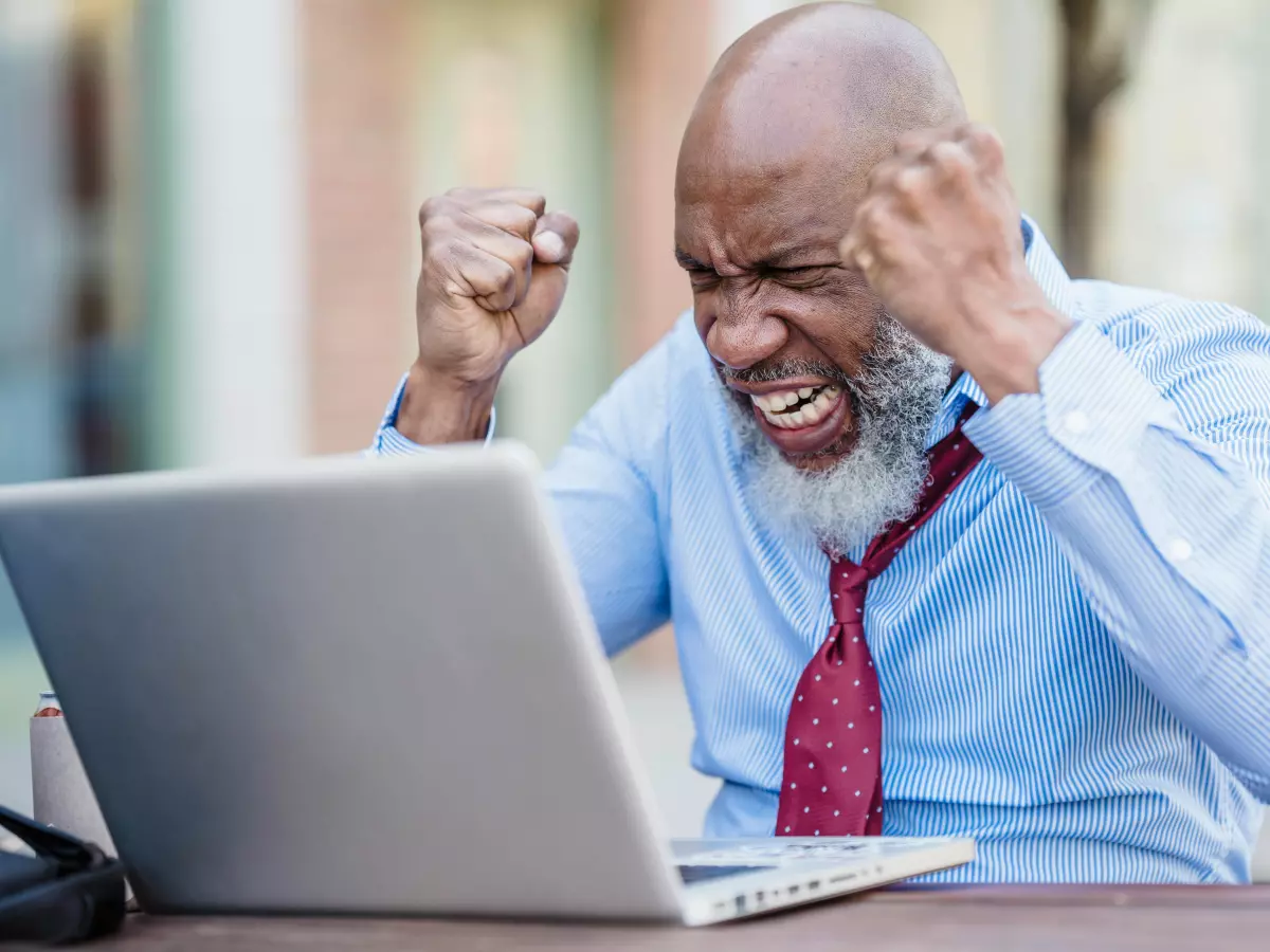 A man sits at a computer, looking frustrated. He is clenching his fists and appears to be angry.