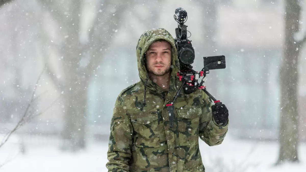 A man in winter clothing holding a camera in snowy weather