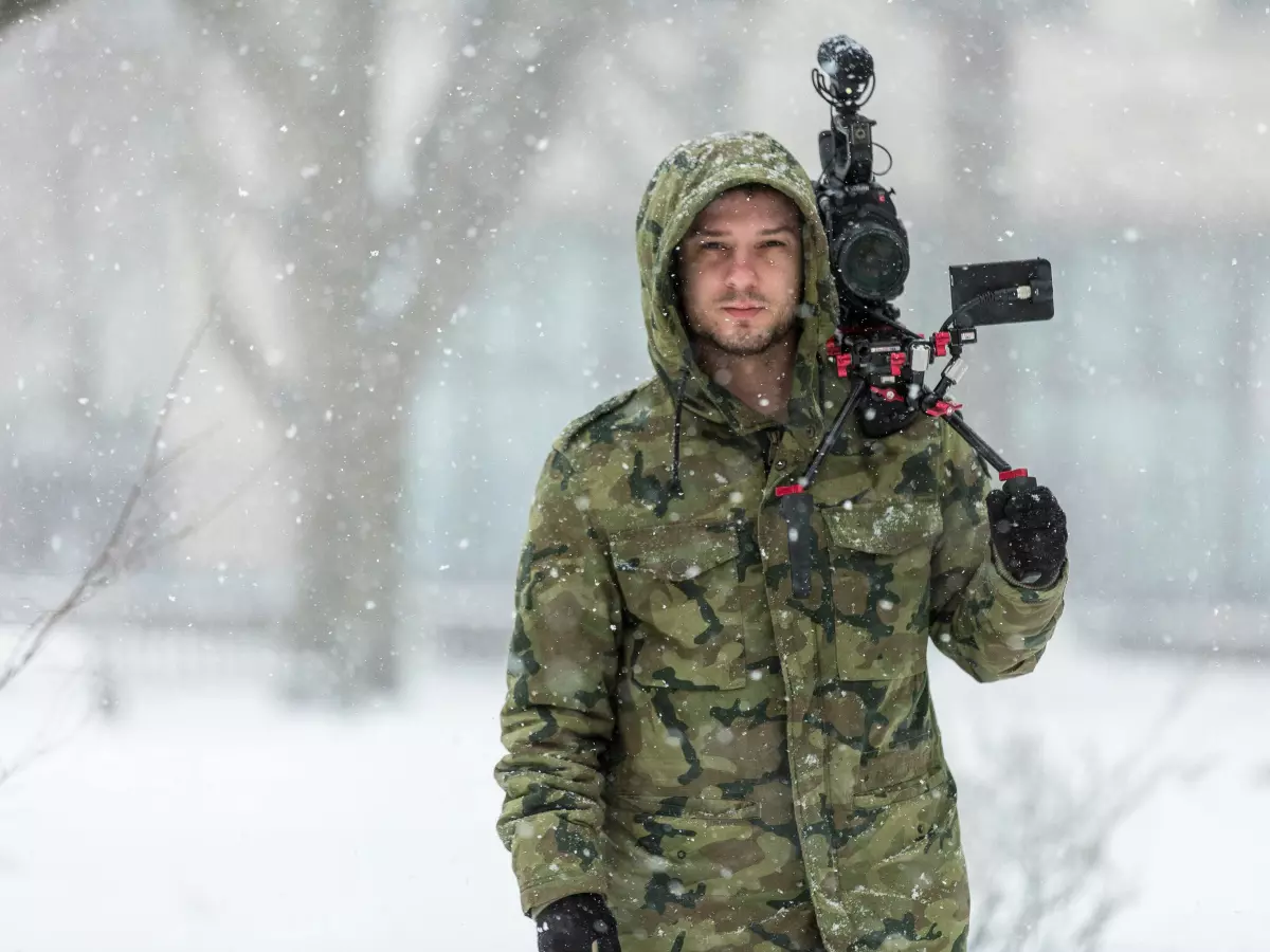 A man in winter clothing holding a camera in snowy weather