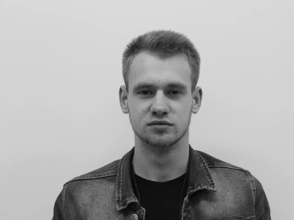 A black and white portrait of a man with short hair wearing a denim jacket.