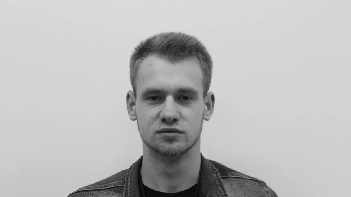 A black and white portrait of a man with short hair wearing a denim jacket.