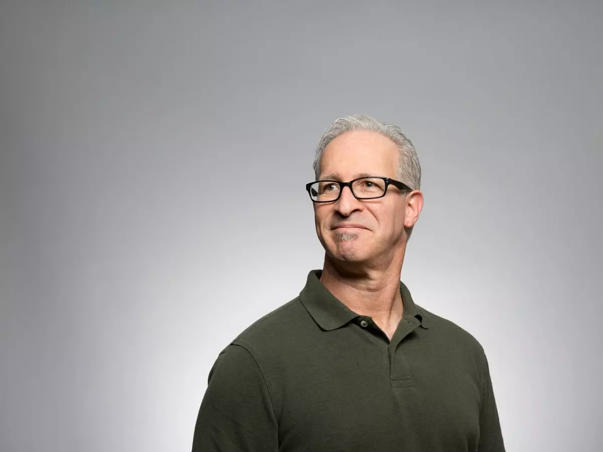 A middle-aged man with gray hair and glasses, looking thoughtfully off-screen, against a plain gray background.