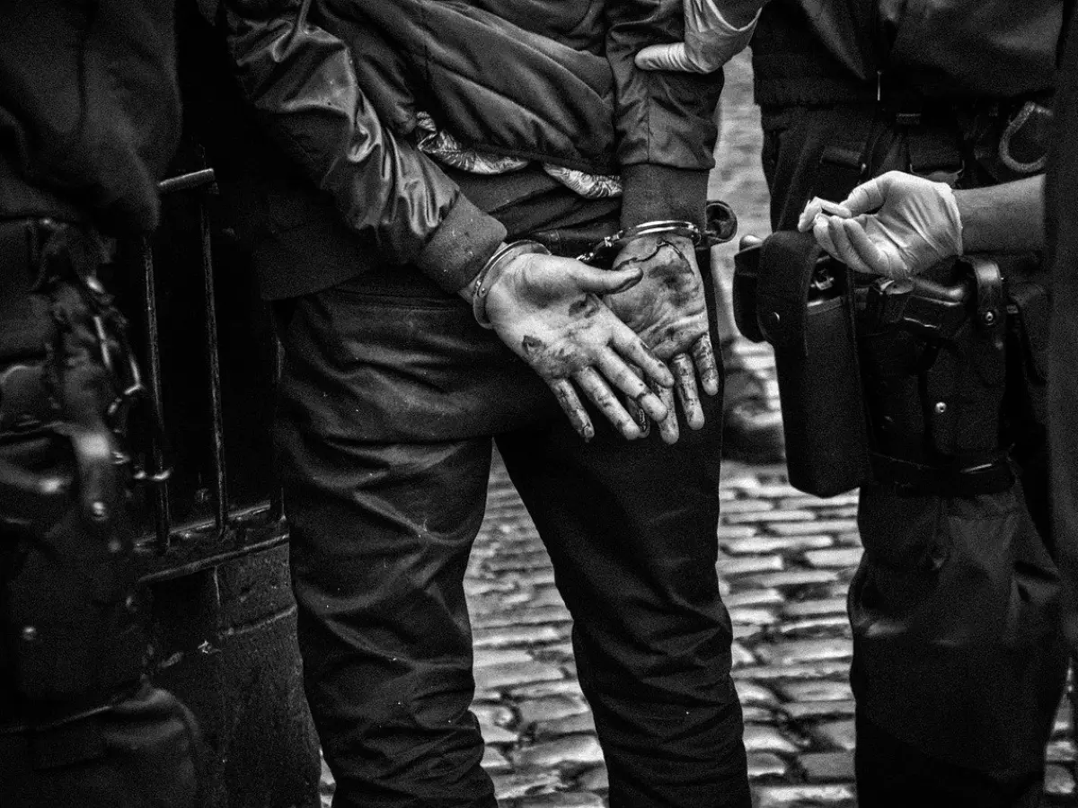 A person in handcuffs, surrounded by police officers.