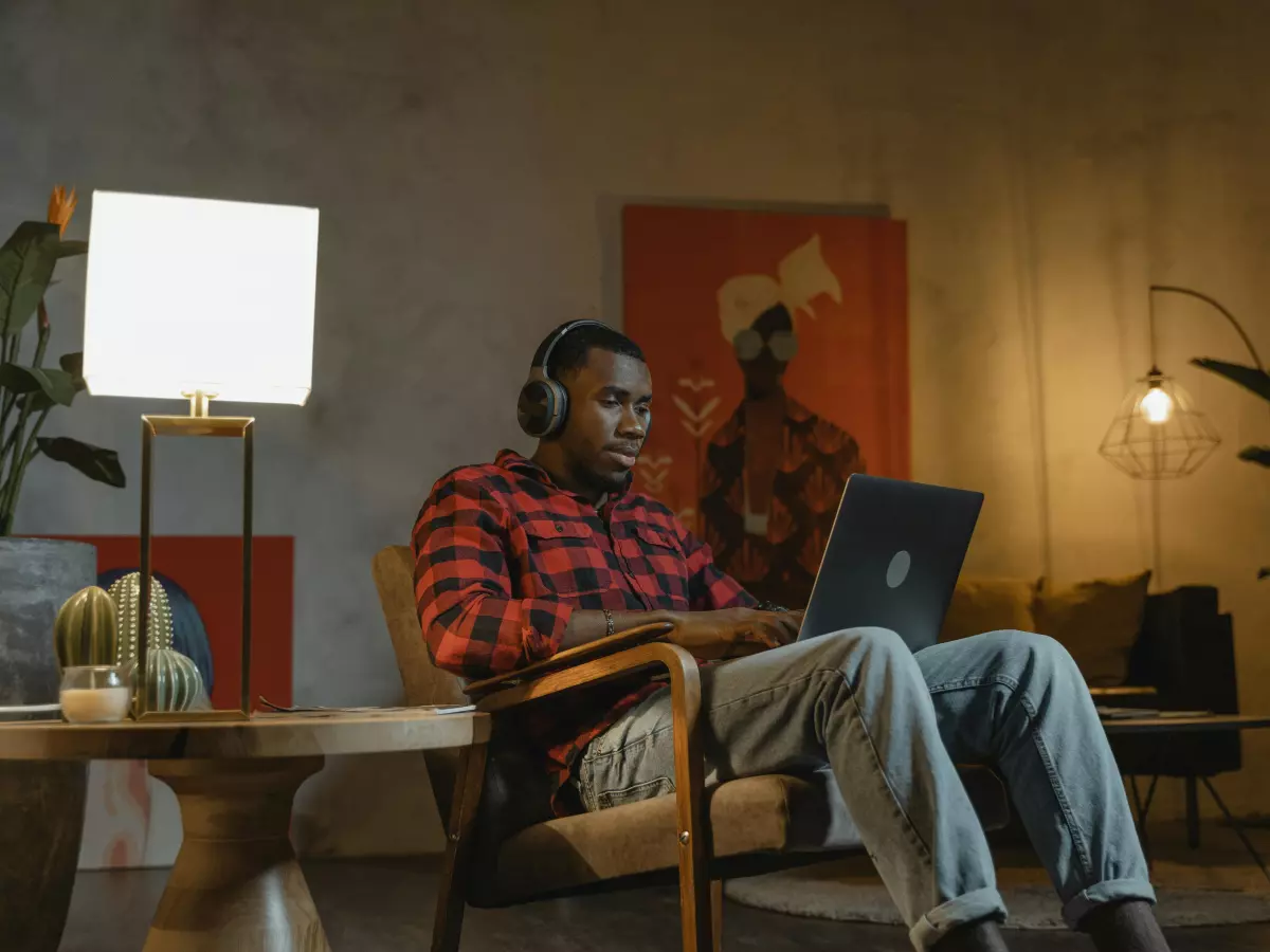 A young man with headphones is looking at a laptop in his home office.