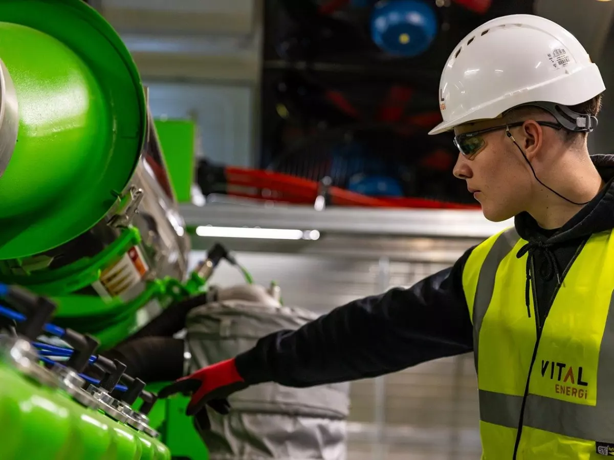 A man wearing a hard hat and safety glasses works in a factory setting.