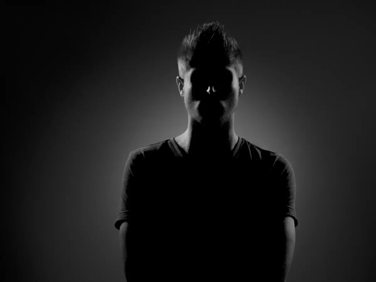 A man standing in front of a dark background, his face partially obscured by shadows.