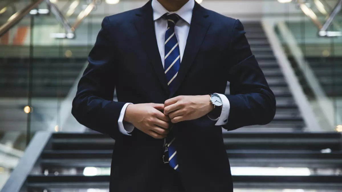 A man in a suit stands on a staircase, adjusting his jacket. The image is well-lit and conveys a sense of professionalism.