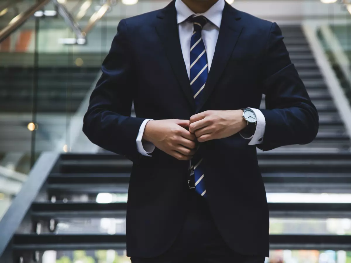 A man in a suit stands on a staircase, adjusting his jacket. The image is well-lit and conveys a sense of professionalism.