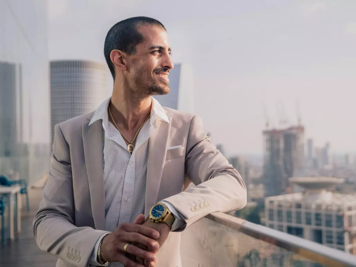 A businessman in a suit stands on a rooftop overlooking a cityscape, looking out over the horizon. The background is blurred and out of focus, while the businessman is in sharp focus. He appears confident and successful. The setting is upscale and modern.