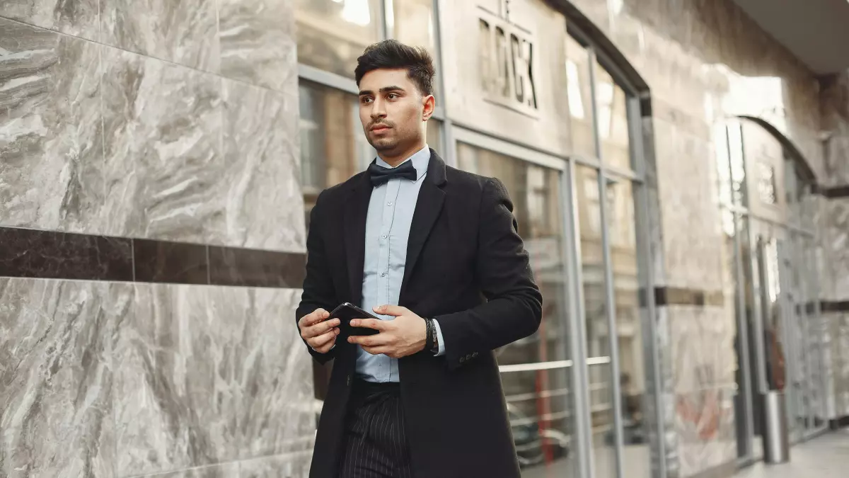 A man in a suit is walking down the street and using his phone.