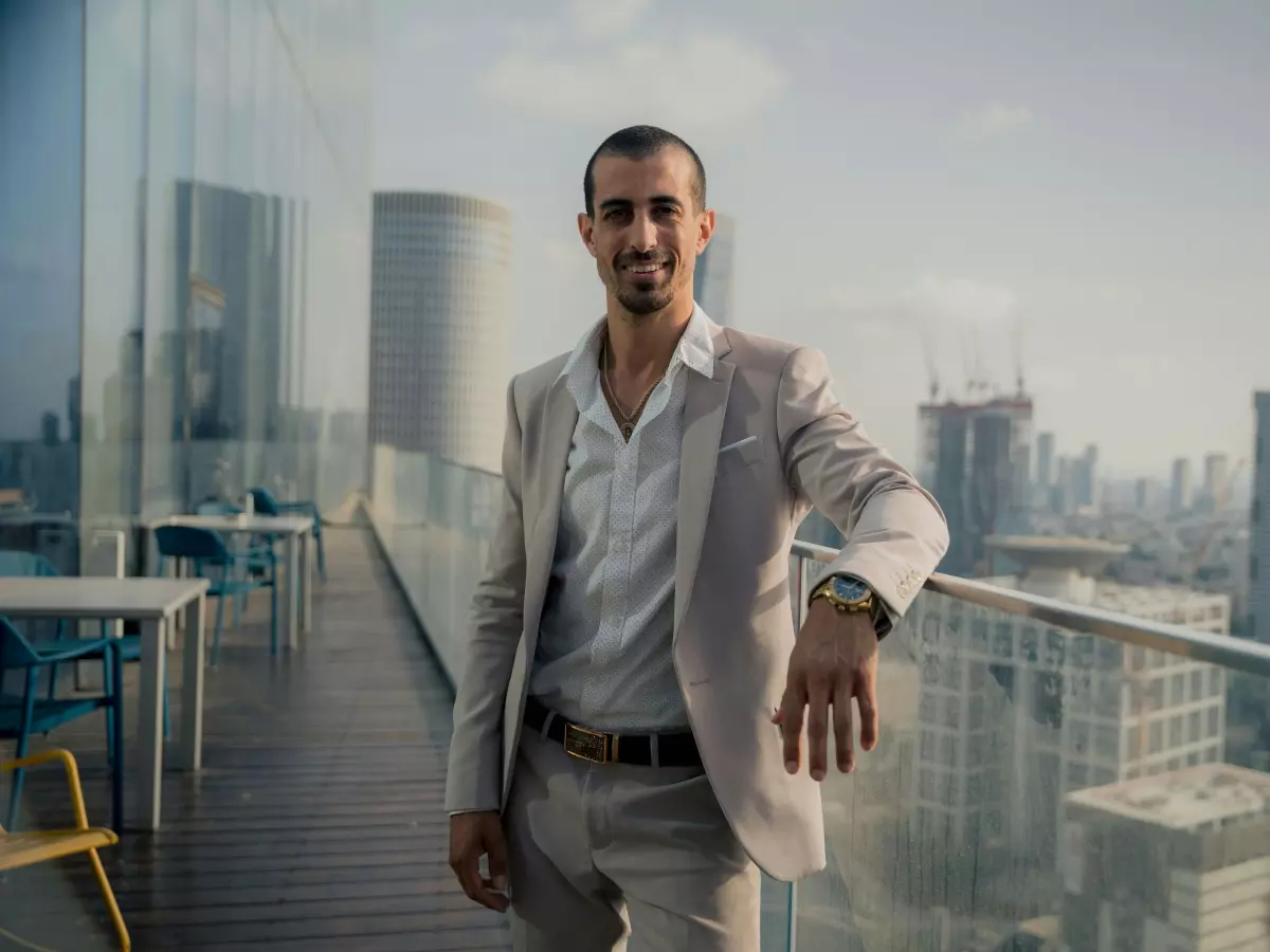 A confident-looking man in a suit stands on a rooftop overlooking a modern city skyline. He appears to be in a position of power.