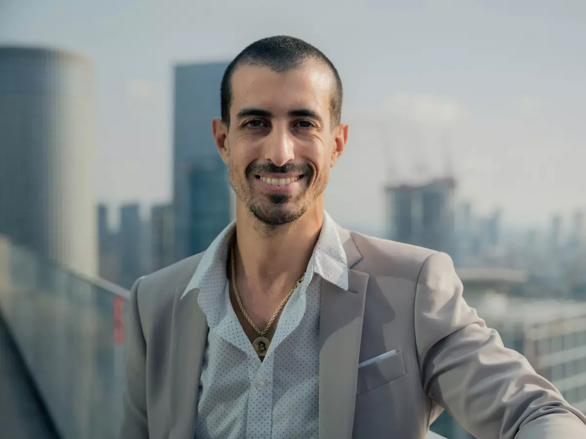 A businessman in a suit is standing on a rooftop overlooking a cityscape. The city is bathed in warm sunlight, and the sky is clear.