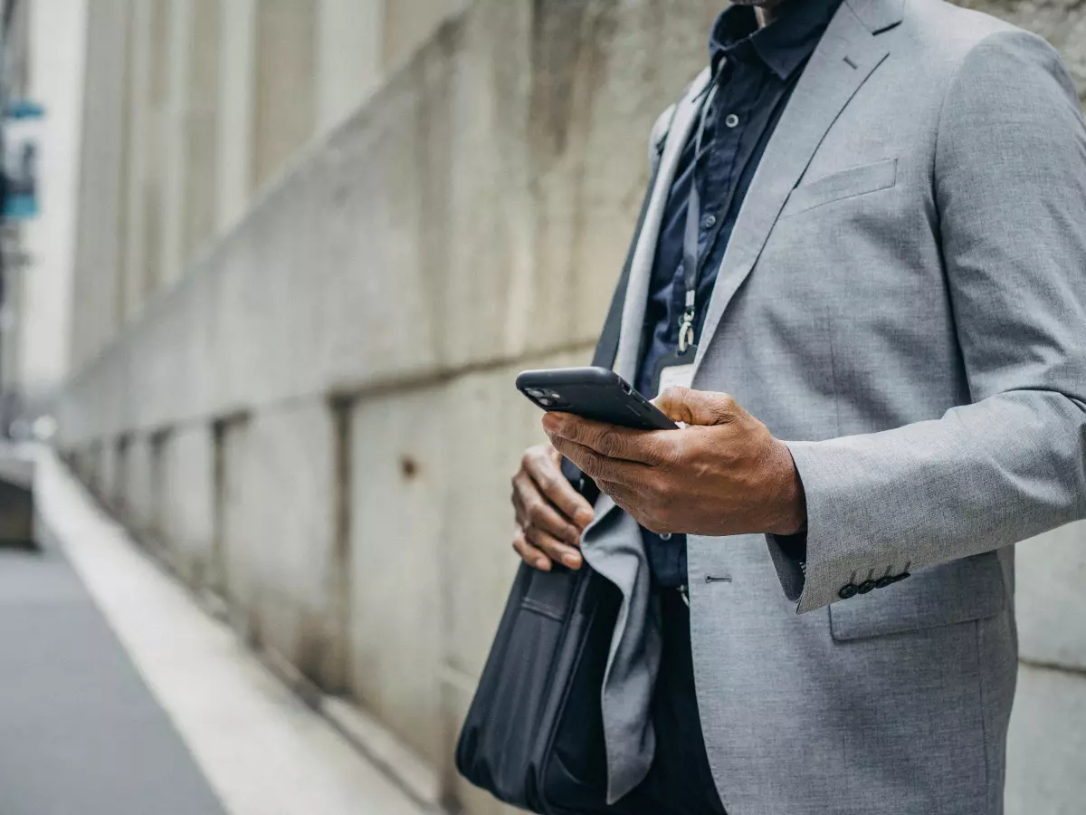 A man in a grey suit is standing on a city street and looking at his phone.