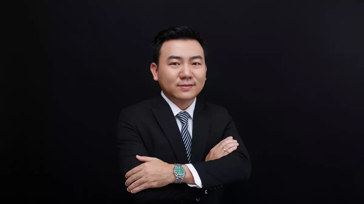 A man in a suit standing with his arms crossed against a black background.