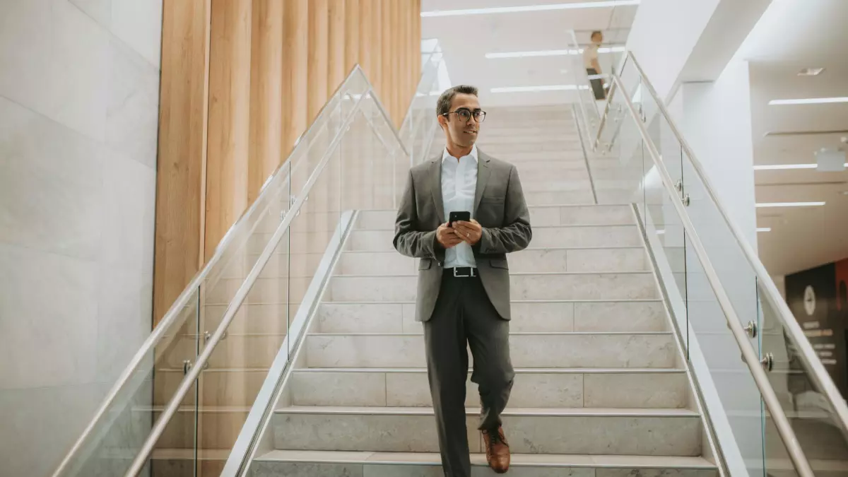 A man in a suit is walking down a staircase while using his smartphone.