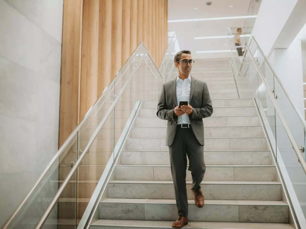 A man in a suit is walking down a staircase while using his smartphone.