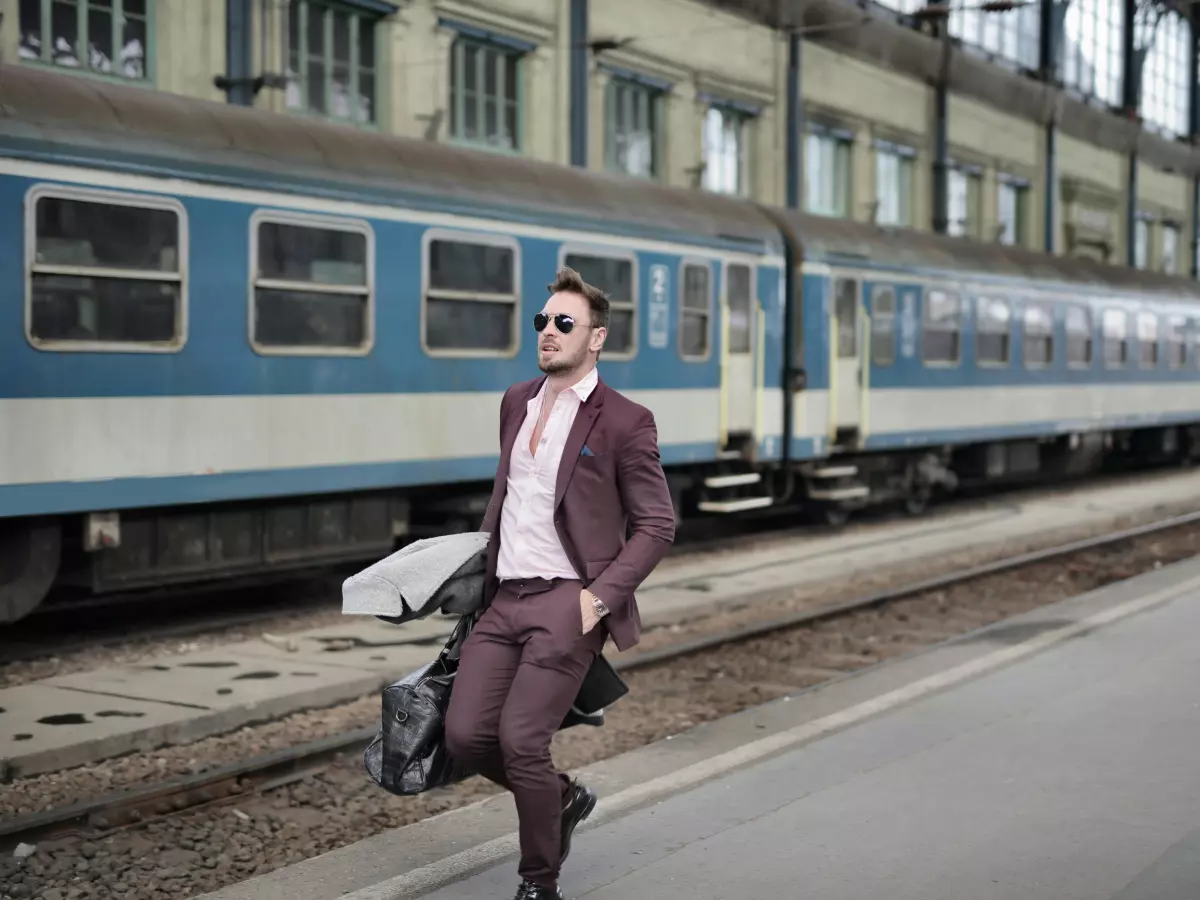 A man wearing a suit with a briefcase is walking on a train platform. He is wearing sunglasses. The train behind him is blurry. 