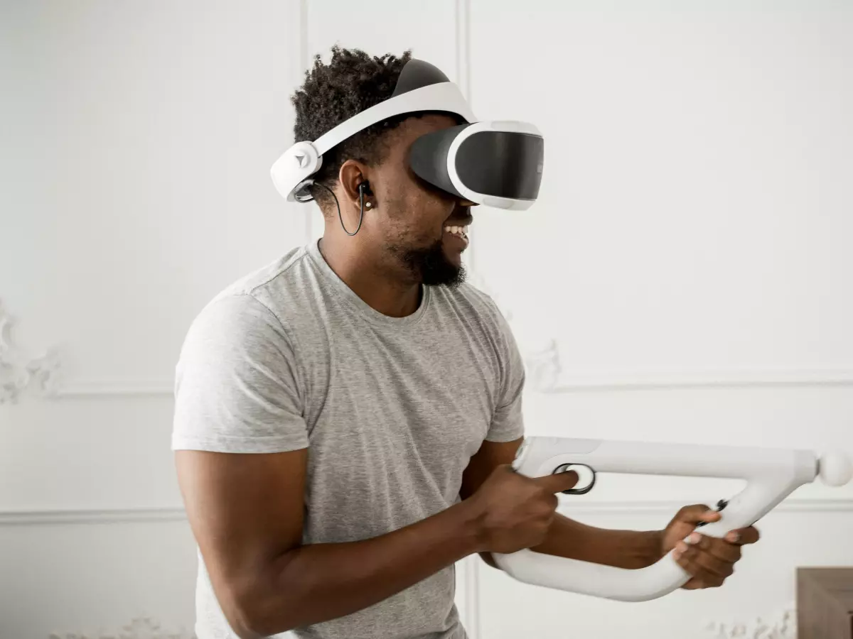 A young man wearing a VR headset and holding two controllers is playing a VR game.