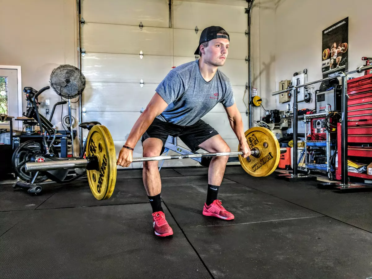 A man is lifting a barbell in a gym setting.