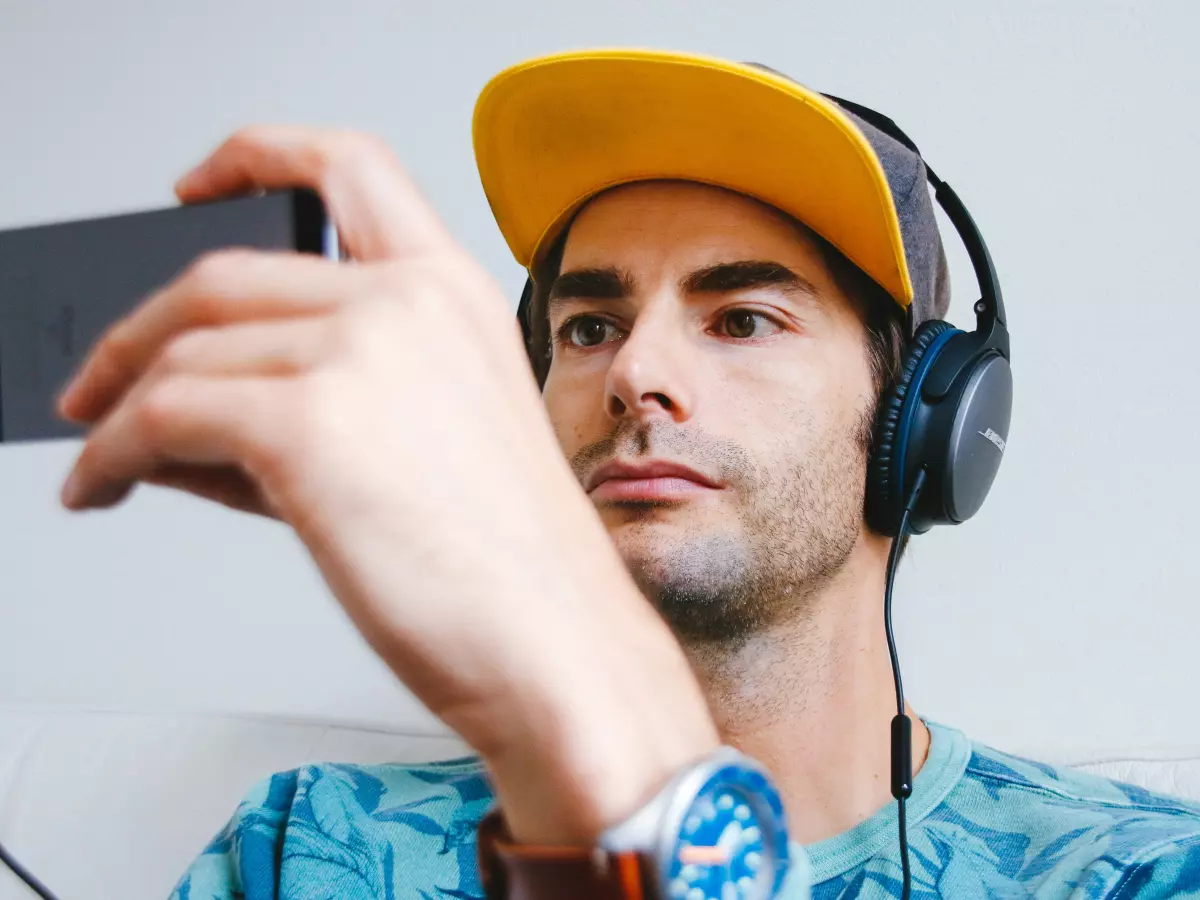 A young man wearing headphones is looking intensely at his smartphone.